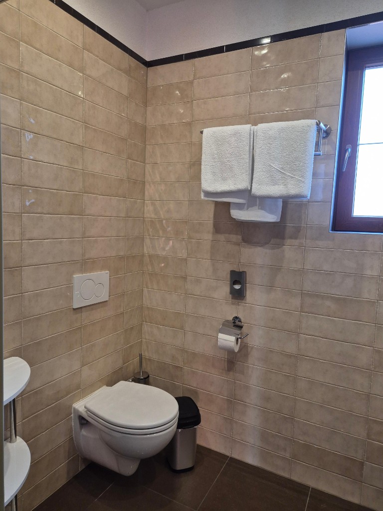 Hygienisch gereinigtes Hotel-WC mit beigen Fliesen und bereitgelegten Handtüchern